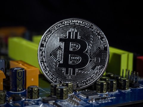 Shiny silver bitcoin virtual crypto currency coin laying on electronic circuit motherboard computer