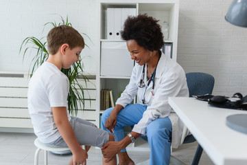 Obraz premium Woman African American doctor general practitioner examining child's patellar knee-jerk reflex