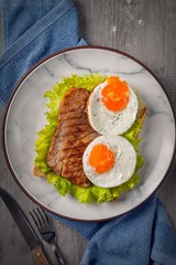 Fried egg and steak on bread for breakfast on plate and rustic table