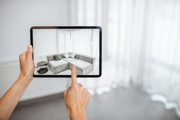 Placing new furniture on a digital tablet into the empty interior, looking how it looks before buying. Concept of augmented reality in design and retail business - obrazy, fototapety, plakaty