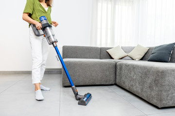 Woman cleaning floor with cordless vacuum cleaner in the modern white living room. Concept of easy...