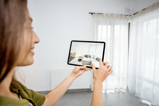 Young woman placing new furniture on a digital tablet into the empty interior, looking how it looks before buying. Concept of augmented reality in design and retail business