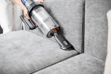 Woman cleaning sofa with a modern cordless vacuum cleaner with a special nozzle, close-up. Dry cleaning concept with wireless vacuum cleaner