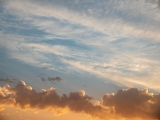 Bright multicolored clouds enlightened with rays of setting sun. Bright blue sky with orange cumulus, stratus and cirrus clouds
