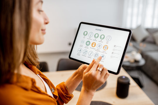 Young woman controlling home with a digital touch screen panel. Concept of a smart home and mobile application for managing smart devices at home