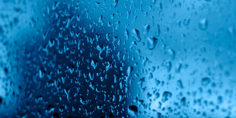 Gorgeous rainy glass with raindrops in classic blue tones. Blurred background with shallow depth of field. Selective focus. Copyspace.