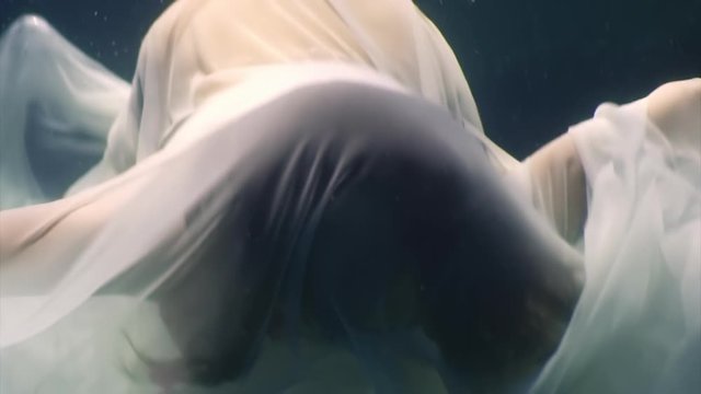 Young woman underwater model in white cloth on background of blue water. Concept of creativity and art of creating images.