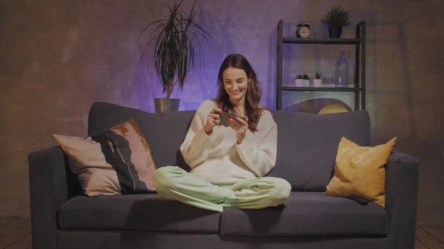 Young mother and son sitting on the couch in a cozy room and playing on the phone