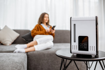 Young woman relaxing on the couch while air humidifier or purifier working on the foreground....
