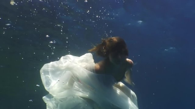 Young woman underwater model in white cloth on background of blue water. Concept of creativity and art of creating images.