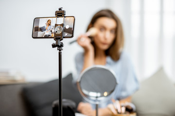 Young woman recording on a smart phone her vlog about cosmetics, showing and demonstrating makeup. Influencer marketing in social media concept