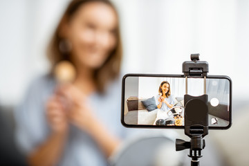 Young woman recording on a smart phone her vlog about cosmetics, showing and demonstrating makeup, close-up on phone. Influencer marketing in social media concept - 308966739