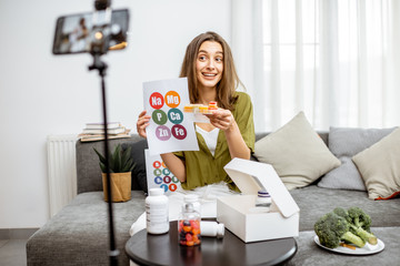 Young woman recording on a smart phone her vlog about healthy eating and nutritional supplements. Preventive medicine and influencer marketing concept