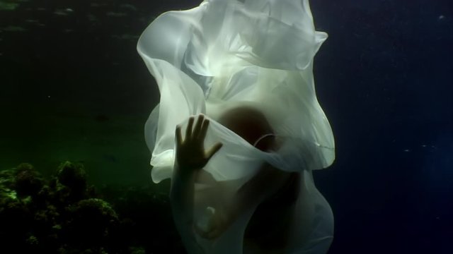 Young woman underwater model in white cloth on background of blue water. Concept of creativity and art of creating images.