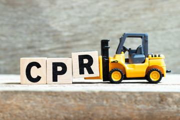 Toy forklift hold letter block R to complete word (abbreviation of Cardiopulmonary resuscitation) on wood background