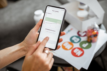 Woman checking the result of medical tests on a smartphone, close-up with nutritional supplements on the background. Concept of individual online selection of food supplements