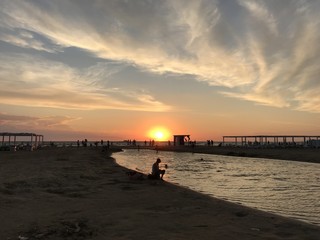 Fototapeta premium Landscape at sunset with silhouettes of people at the confluence of the river in the sea. Mobile photo in natural evening light. Russia Anapa. 