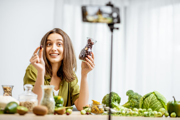 Young woman recording on a smart phone her vlog about healthy eating. Sitting at the table with...