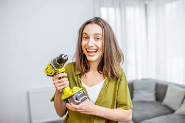 Portrait of a young and happy handywoman with cordless screwdriver at home. Concept of an easy...