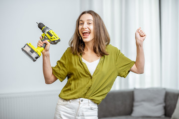 Portrait of a young and happy handywoman with cordless screwdriver at home. Concept of an easy household work with modern working tools