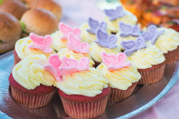 Close-up of red velet cupcakes with white cream cheese on top decorated with colorful butterflies. Catering for burthday party.