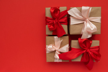 Gift boxes wrapped brown craft paper and red and pink ribbon on red background. Valentines day or Christmas celebration concept. Top view