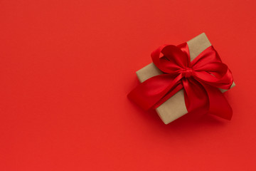 Gift box wrapped brown craft paper and red ribbon on red background. Valentines day or Christmas celebration concept. Top view