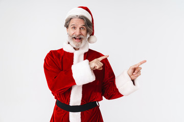 Fototapeta na wymiar Image of bearded gray-haired Santa Claus man in red costume pointing fingers aside at copyspace