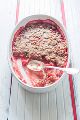 Crunchy strawberries crumble, top view, halfserved, on an oval serving dish, on a  white background