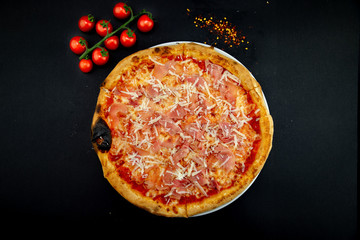 Isolated round pizza on black background with tomatoes