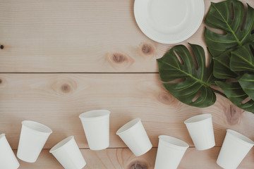 Paper food packaging, eco friendly disposable, compostable, recyclable paper cups and plate with plant branches on wooden background. copy space top view. zero waste concept