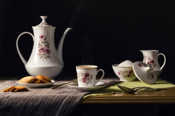 Vintage porcelain tableware with floral ornaments with hot coffee, sugar and cookies on tablecloths on a rustic wooden table. Classic and traditional lifestyle. Space for text. Dark photo