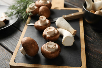 Champignons, eringi, dill, knife and board on wooden table, close up