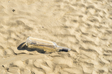 Junk glass wine bottle on sand beach in the sun, concept of sea or oceanic waste