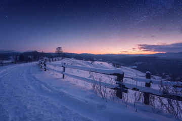 Amazing nature mountains landscape, winter path at night with snow and beautiful blue sky with stars and glow of sunset, outdoor travel background