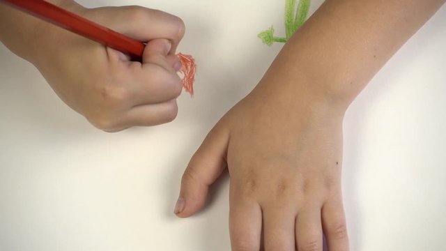 A picture of a child on paper. The view from above, the child draws in colored pencils.