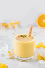 lassi drink mango close-up on a light concrete background next to a slice of orange and ice. traditional indian drink
