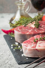 Fresh veal shank slices beef meat for Osso Buco cooking on cutting board with ingredients and seasonings thyme, pepper, salt.