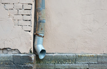 A fragment of the plastered facade of an old building with a drainpipe and partially exposed...