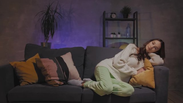A young woman is sitting on a sofa in a cozy room watching TV