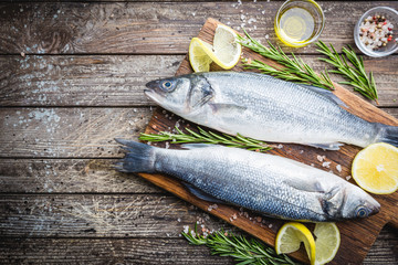 Fresh raw seabass and ingredients for cooking. Two fish seabass with lemon, spices and herbs on wooden table, top view with copy space.