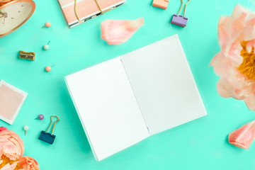 Obraz premium Empty Notebook for writing Dreams and Ideas, with different Stationery, and Big Pink Peony flowers laying on Green background. Top View. Idea of Girly Office settings. Flat lay style.