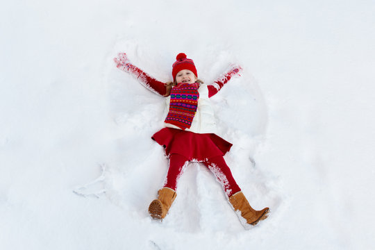 Child making snow angel. Kids winter outdoor fun.