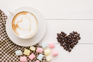 a cup of Latte Art coffee, design with marshmallow, heart-shaped love on fabric and roasted coffee beans on a white wooden table leaving space for your text. Top view