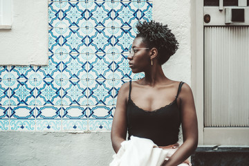 Portrait of a young charming African female in spectacles and a tank top standing next to the wall...