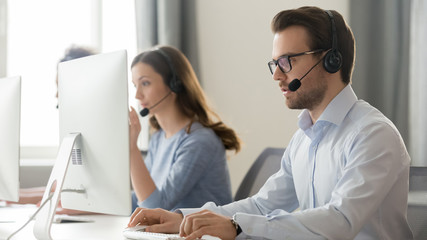 Male employee in headset with microphone work on pc