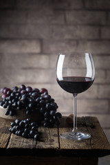 Red wine in a glass and ripe grapes on wooden table