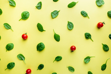 Spinach leaves and tomato pattern background on yellow, top view