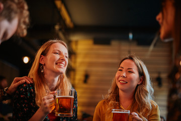 Group of friends drinking beer, chatting and talking to barman. Night out. Pub interior.