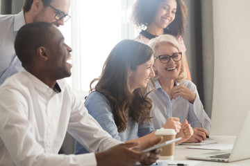 Smiling multiethnic employee laugh watching funny video on laptop